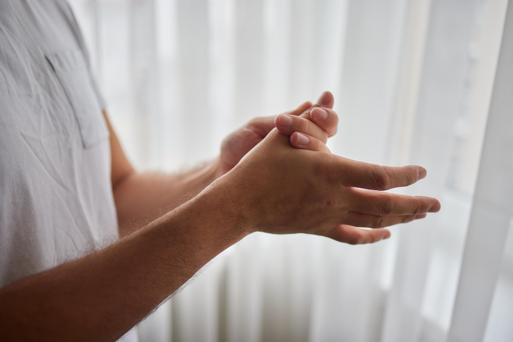 Fingertips pressed together indoors near sheer white curtains.